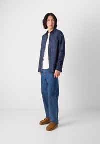Camisa de botones con estampado náutico sobre una camiseta blanca, combinada con jeans azul claro y zapatos de mocasín marrones.