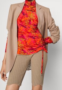 Ljusa blommönstrade toppar i röd och orange nyanser, kombinerad med beige ribbade shorts. Blazern är ljusbrun, med en texturerad yta och skräddarsydd passform.