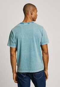 Tyrkysové tričko s krátkým rukávem s mírně vybledlým vzhledem. Šití detailu na rukávech, kulatý výstřih a štítek na zadní straně.