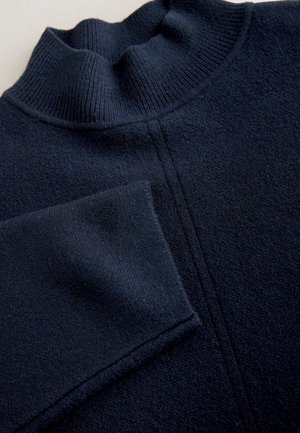 Dunkel marineblauer Strickpullover mit einem Rippenrollkragen und sichtbaren Nahtdetails, die vertikal über die Vorderseite verlaufen.