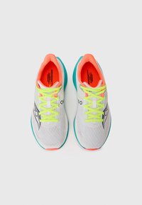 Pair of white running shoes with neon yellow laces, bright orange inner lining, teal soles, and black logo viewed from above on a white background.