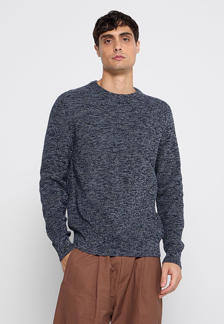 Marinefarbener Strickpullover mit Rundhalsausschnitt, strukturiertem Stoff und langen Ärmeln. Lockerer Schnitt, kombiniert mit braunen weit geschnittenen Hosen.