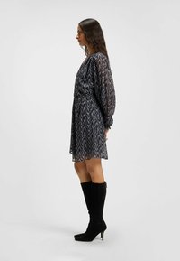 Abito scuro a fantasia con maniche lunghe, vita stretta e orlo a campana. Indossato con stivali neri in suede al ginocchio e una texture liscia.