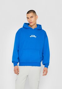 Modra kapuca narejena iz mehke tkanine z sprednjim žepom, na kateri je napisano "YOUTH" v belem. Oversized oblikovanje z zatezno kapuco.