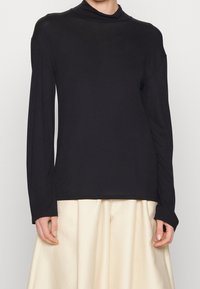 Maglietta nera a maniche lunghe con collo alto, realizzata in tessuto morbido con una vestibilità comoda. Presenta una texture liscia e spalle leggermente scese.