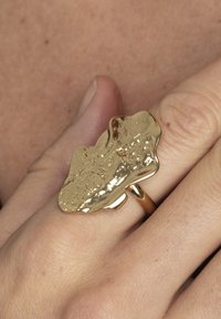 Gouden ring met een gemarmerde, organische vorm en een glanzend, reflecterend oppervlak. De band is smal en rond, wat de uniciteit van het ontwerp benadrukt.