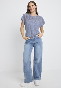 Blue and white striped short-sleeve shirt with a round neckline, paired with light blue wide-leg jeans and white sneakers.