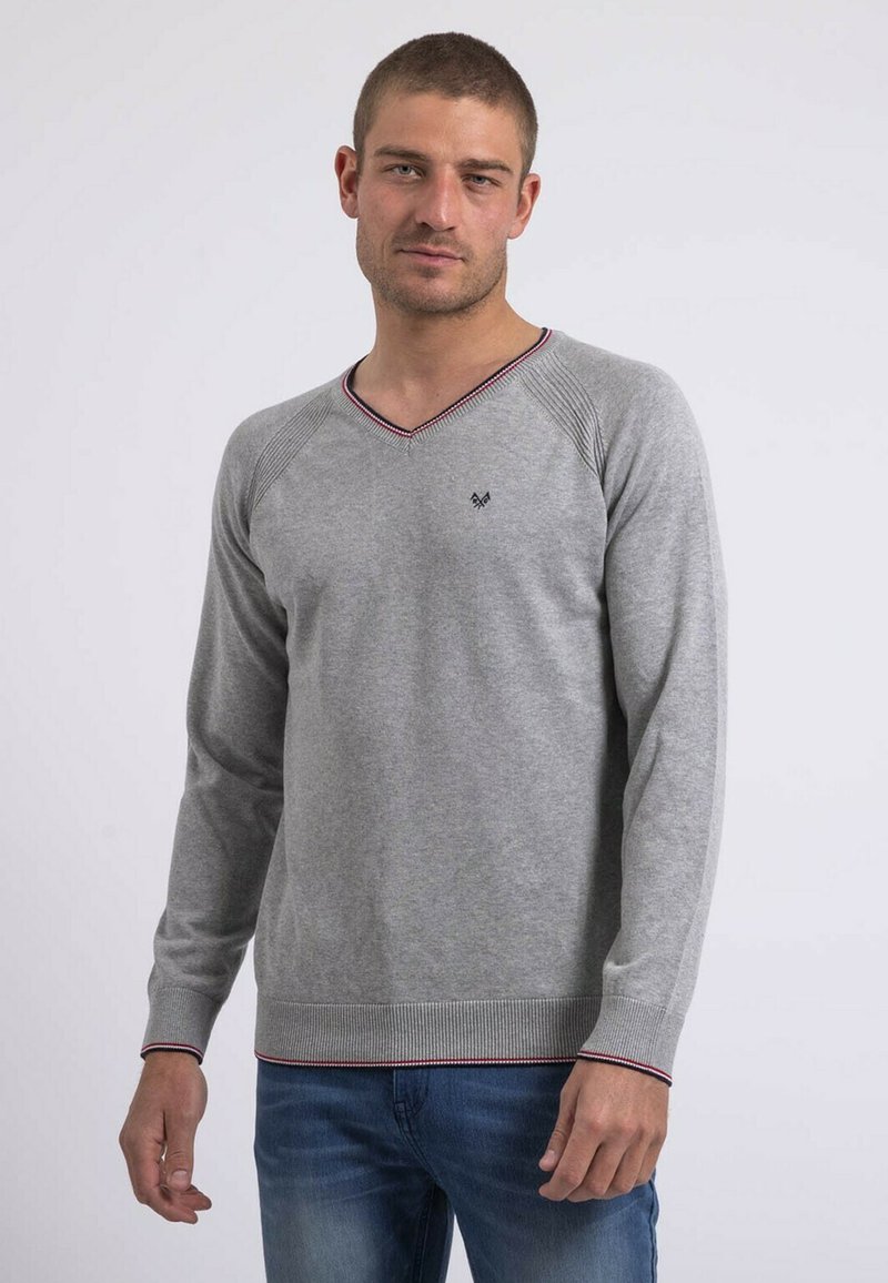 Pull gris à col V avec manches raglan, présentant un tricot texturé et un ourlet côtelé avec des accents rouges et marine. Logo sur la poitrine.