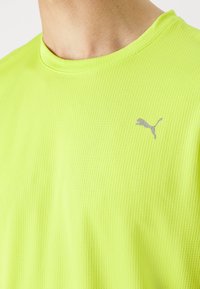 Svítivě neonově žluté sportovní tričko s žebrovanou texturou, na levé horní straně hrudi s malým šedým logem Puma.