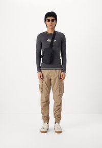 Long-sleeve gray top with white accents, beige cargo pants with side pockets, and a black crossbody bag. Tan shoes with a white base.