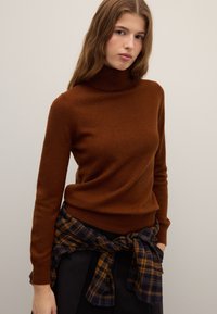 Brown turtleneck sweater in soft fabric, fitted design. Paired with a navy and yellow plaid flannel tied at the waist. Smooth texture.