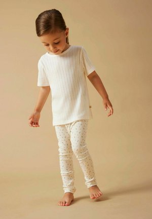 Cremefarbene, gerippte, kurzärmelige Bluse kombiniert mit cremefarbenen Leggings mit Blumenmuster, beide aus weichem, dehnbarem Stoff gefertigt.