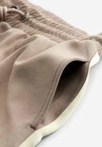 Shorts beiges en tissu doux, dotés d'une taille élastique, d'un cordon de serrage, et d'une bordure blanche le long de l'ourlet. Présente un détail de poche intérieure.