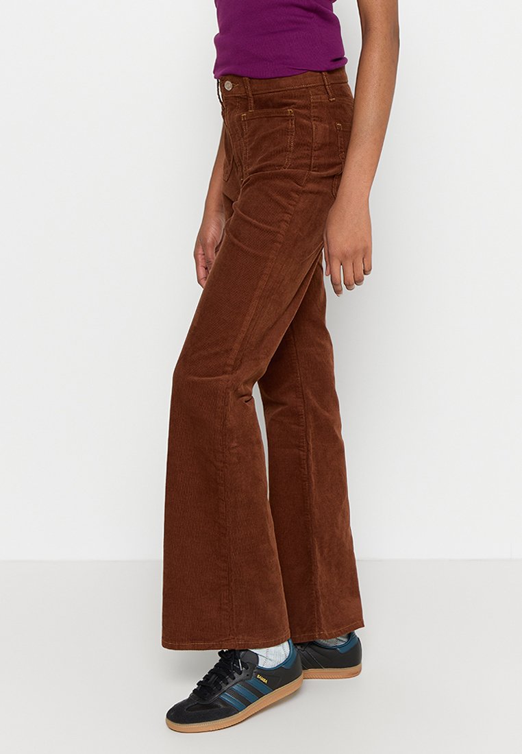 Braune Corduroy-Hosen mit Schlag, vorn Taschen und feiner Struktur. Kombiniert mit schwarzen Sportschuhen mit blauen Streifen und Gummisohlen.