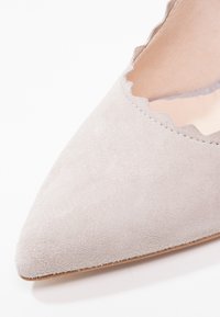 Gros plan sur une chaussure en daim gris clair à bout pointu avec un bord festonné le long de l'ouverture.