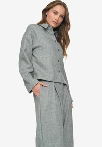 Blazer en gris tissé avec un devant à boutons et un col, associé à un pantalon large plissé assorti. Tissu texturé, coupe décontractée.