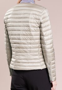 Light gray puffer jacket with horizontal quilted design, two zippered side pockets, and a fitted silhouette. Smooth, shiny texture.