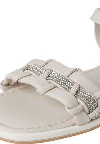 Sandales beige clair avec un design tissé, ornées d'une rangée de strass le long de la bride. Texture en cuir lisse et semelle plate.
