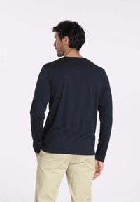 Chemise à manches longues navy, col rond, fabriquée en tissu doux. Présente un design simple, une texture lisse et une silhouette ajustée.