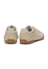 Beige Sneaker mit glatter, wildlederähnlicher Textur, abgerundeter Form, kontrastierenden Sohlen aus Kautschuk in Gummifarben und dezentem, geprägtem Branding an der Ferse.