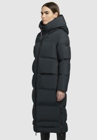 Cappotto lungo nero felpato con colletto alto, chiusura con zip e tasche laterali. Presenta sezioni trapuntate e un cappuccio, realizzato in un materiale liscio e resistente all'acqua.