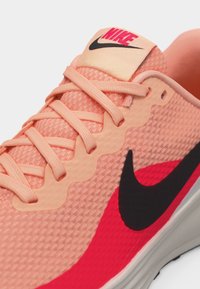 Κοντινή λήψη ενός αθλητικού παπουτσιού Nike σε κοραλλί ροζ, με ροζ κορδόνια, υφασμάτινη υφή, μαύρο λογότυπο Swoosh και κόκκινες λεπτομέρειες στο πλάι.