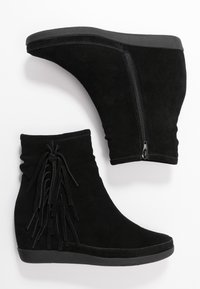 Černé semišové kotníkové boty na klínovém podpatku, s bočním zipem a třásněmi na jedné straně. Hladký materiál a zaoblený tvar špičky.