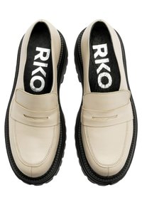 Beżowe sk órzane mokasyny z czarną gumową podeszwą, z dekoracyjnym paskiem i logo RKO na czarnej wkładce. Gładka tekstura.