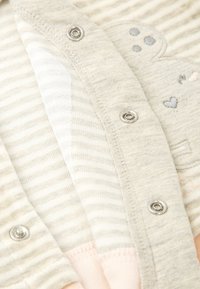 Cardigan gris claro que presenta texturas a rayas y lisas, botones metálicos y acentos bordados de corazones y huellas de patas en colores pastel.