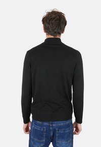 Maglione nero lavorato a maglia con collo alto, maniche lunghe e orlo a coste. Indossato con jeans di denim blu, che mostrano una vista posteriore casual.