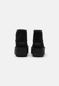 Botines de ante negro con un diseño de caña alta, cuello acolchado y suela de goma gruesa. Presentan una marca en la parte trasera.