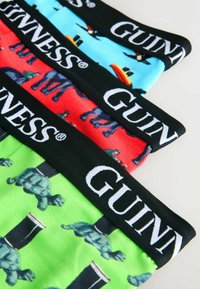 Drei Paare bunte Boxershorts mit Schildkröten- und Guinness-Glas-Motiven, jeweils mit schwarzen Bundbändern, auf denen "GUINNESS" in Weiß steht.