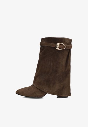 Bruine suède enkellaars met een spitse neus, gevouwen design en een zijband met een gouden gespaccent. Platte hak.