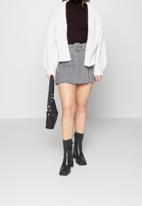 Cardigan bianco in maglia, dolcevita marrone, mini gonna a quadri bianca e nera, stivali neri con tacco e borsa a spalla nera.