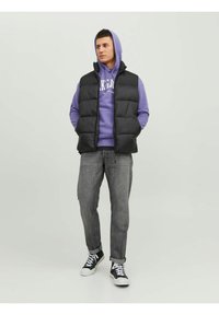 Black puffer vest over a purple hoodie, paired with grey jeans and black sneakers. The vest features a high collar and quilted design.