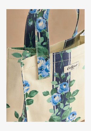 Tote torba z vzorcem v bež barvi z moderim cvetličnim motivom in zelenimi listi, ki ima vertikalne mornarsko modre črte in blagovno znamko. Teksturovana tkanina.