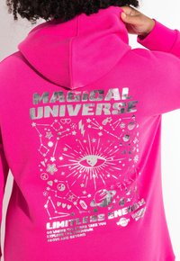 Felpa rosa brillante con testo argento metallico e grafiche cosmiche, tra cui stelle e un occhio, con una vestibilità comoda.