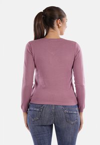 Maglione fitted a maniche lunghe in morbido tessuto knit mauve, con scollatura a girocollo e polsini a coste, abbinato a jeans blu scuri con tasche posteriori.