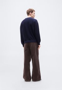 Πλεκτό πουλόβερ σε ναυτικό μπλε με ριμπ στρίφωμα και μανσέτες, συνδυασμένο με καφέ παντελόνι κορντό κουλός με φαρδιά πόδια, πίσω τσέπες και άνετη εφαρμογή.