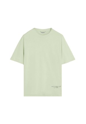 Camiseta de manga corta de color verde claro con escote redondo y pequeño texto en cursiva cerca del bajo derecho.