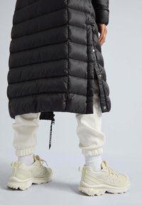 Sort puffjakke med quiltet mønster og trykknaplukninger, parret med hvide sweatpants med opkravede manchetter og beige chunky sneakers med teksturerede detaljer.
