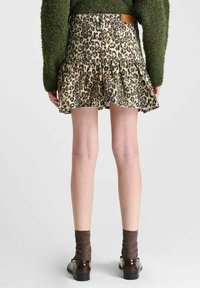 Leopardprint spijkerrok met een uitlopende ontwerp, voorzien van een gelaagd zoom en een bruine leren label aan de achterkant, gecombineerd met donkere schoenen en sokken.