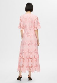 Rochie roz din dantelă, cu modele florale, mâneci scurte și un tiv în straturi. Finalizată cu o talie ajustată și o siluetă lejeră. Sandale cu toc negre.