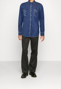 Camicia di jeans con una tonalità di blu scuro, design con bottoni, e due tasche frontali, arricchita da cuciture a contrasto e colletto a punta.