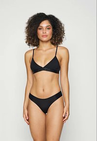 Črn bikini komplet, ki vključuje trikotno bralette in nizke hlačke. Gladka tekstura in minimalističen dizajn s tankimi naramnicami. Brez vzorcev ali dodatkov.