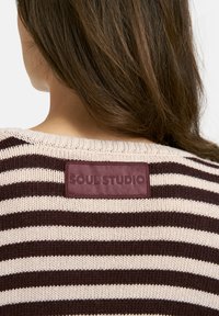 Strickpullover mit horizontalem Streifenmuster in Off-White und Dunkelbraun, ausgestattet mit einem braunen Lederpatch mit dem eingeprägten "SOUL STUDIO" auf der Rückseite.
