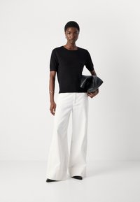 Black knit short-sleeve top with a round neckline paired with high-waisted white wide-leg trousers and a black leather clutch.