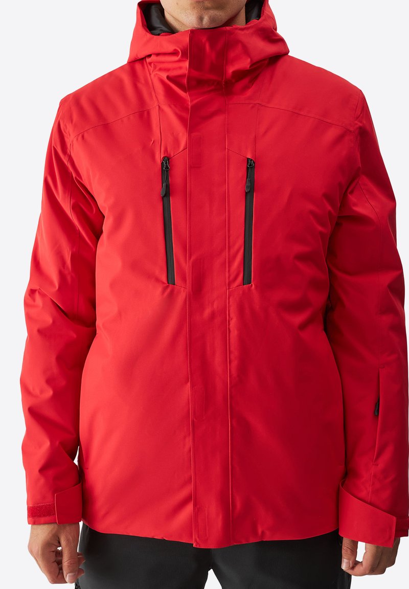Giacca isolante rossa con colletto alto, cappuccio regolabile, due tasche sul petto con zip e polsini in velcro. Esterno liscio e impermeabile.