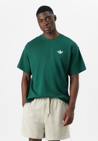 Tricou verde din bumbac, cu mâneci scurte și guler circular ribanat, având un mic logo crem. Asortat cu pantaloni scurți bej deschis, cu un model.