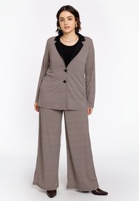 Geruit pakken in gedempte tinten met een lange blazer met zwarte revers en wijde broekspijpen, beide gemaakt van een soepele stof.